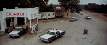 Movie still from “The Sugarland Express” (1974), directed by Steven Spielberg – A police car parked in front of a gas station; Extreme Wide shot, High angle