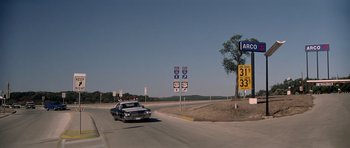 Movie still from “The Sugarland Express” (1974), directed by Steven Spielberg – A car driving down a road near a street sign; Wide shot, High angle