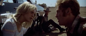 Movie still from “The Sugarland Express” (1974), directed by Steven Spielberg – A group of people sitting on the ground in a field; Medium shot, Low angle