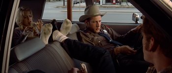 Movie still from “The Sugarland Express” (1974), directed by Steven Spielberg – A man sitting in the back seat of a car wearing a cowboy hat; Medium shot, Low angle