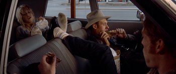 Movie still from “The Sugarland Express” (1974), directed by Steven Spielberg – A man sitting in the back of a car eating pizza; Wide shot, Low angle