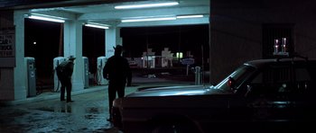 Movie still from “The Sugarland Express” (1974), directed by Steven Spielberg – A man standing in a parking lot next to a car; Wide shot, Over the shoulder angle