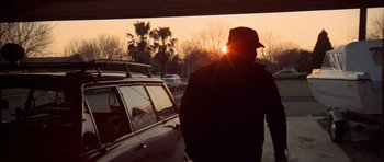 Movie still from “The Sugarland Express” (1974), directed by Steven Spielberg – A man standing in front of a car at sunset; Medium shot, Low angle