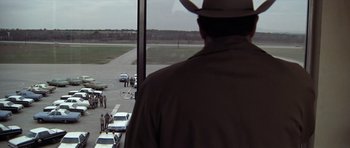 Movie still from “The Sugarland Express” (1974), directed by Steven Spielberg – A man wearing a hat looking out of a window at an airport; Extreme Wide shot, Over the shoulder angle