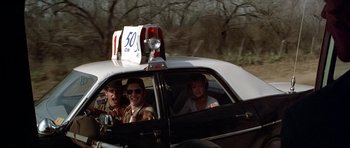 Movie still from “The Sugarland Express” (1974), directed by Steven Spielberg – A group of people riding in the back of a police car; Wide shot, Over the shoulder angle
