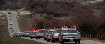 Movie still from “The Sugarland Express” (1974), directed by Steven Spielberg – A line of police cars driving down a street; Extreme Wide shot, Low angle