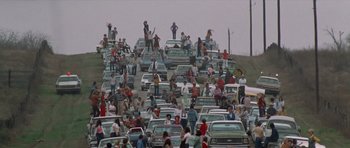 Movie still from “The Sugarland Express” (1974), directed by Steven Spielberg – A large group of people standing in the middle of a street; Extreme Wide shot, High angle