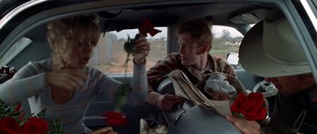 Movie still from “The Sugarland Express” (1974), directed by Steven Spielberg – A man and a woman sitting in the back of a car holding roses; Medium shot, Over the shoulder angle