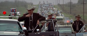 Movie still from “The Sugarland Express” (1974), directed by Steven Spielberg – A man in a suit and cowboy hat in the back of a car; Medium shot, Low angle