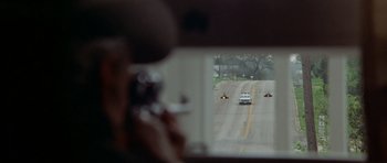Movie still from “The Sugarland Express” (1974), directed by Steven Spielberg – A person taking a picture of a car on the road; Wide shot, Over the shoulder angle