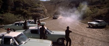 Movie still from “The Sugarland Express” (1974), directed by Steven Spielberg – A group of men standing next to parked cars on the side of a road; Extreme Wide shot, High angle