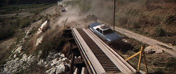 Movie still from “The Sugarland Express” (1974), directed by Steven Spielberg – A car is driving over a bridge on a dirt road; Wide shot, High angle