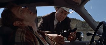 Movie still from “The Sugarland Express” (1974), directed by Steven Spielberg – A man in a cowboy hat is holding a gun; Medium shot, Over the shoulder angle