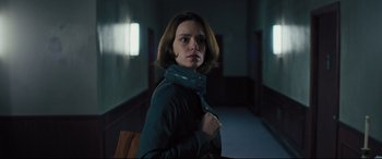 Movie still from “The Super” (2017), directed by Stephan Rick – A woman in a green jacket standing in a room; Medium shot, Low angle