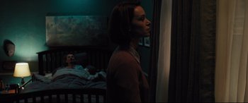 Movie still from “The Super” (2017), directed by Stephan Rick – A woman standing next to a bed in a dark room; Medium shot, Over the shoulder angle