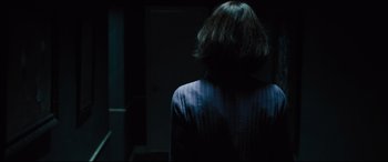 Movie still from “The Super” (2017), directed by Stephan Rick – A person with short hair is standing in a dark room; Medium shot, Over the shoulder angle