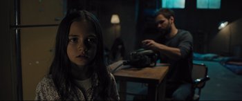 Movie still from “The Super” (2017), directed by Stephan Rick – A young girl standing in front of a man in a dark room; Medium shot, Over the shoulder angle
