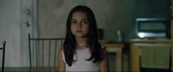 Movie still from “The Super” (2017), directed by Stephan Rick – A little girl with long dark brown hair and blue eyes looking at the camera; Close Up shot, High angle