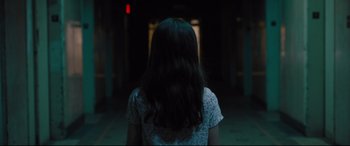 Movie still from “The Super” (2017), directed by Stephan Rick – A woman with long hair is standing in a dark room; Medium shot, Over the shoulder angle