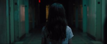 Movie still from “The Super” (2017), directed by Stephan Rick – A woman with long hair standing in a dark room; Medium shot, Over the shoulder angle