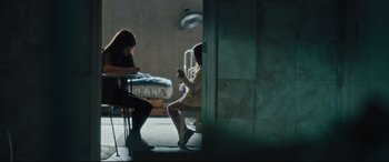 Movie still from “The Super” (2017), directed by Stephan Rick – Two women sitting at a table in front of a bed; Wide shot, High angle