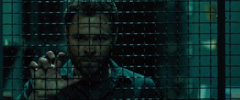 Movie still from “The Super” (2017), directed by Stephan Rick – A man is behind a metal fence looking at the camera; Close Up shot, Overhead angle
