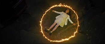 Movie still from “The Super” (2017), directed by Stephan Rick – A young girl laying on the ground in a ring of fire; Wide shot, Overhead angle
