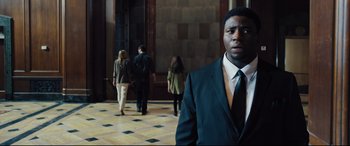 Movie still from “The Super” (2017), directed by Stephan Rick – A man in a suit standing in front of a group of people; Medium shot, Over the shoulder angle