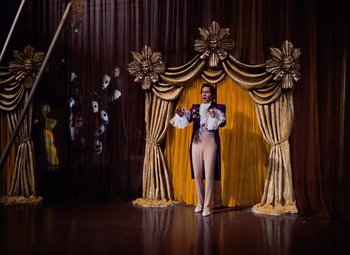 Movie still from “The Tales of Hoffmann” (1951), directed by Michael Powell – A man standing in front of a stage with gold drapes; Wide shot, Low angle