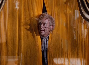Movie still from “The Tales of Hoffmann” (1951), directed by Michael Powell – A man with a face mask looking out of a window; Medium shot, Low angle
