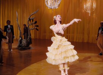 Movie still from “The Tales of Hoffmann” (1951), directed by Michael Powell – A woman in a yellow dress dancing in front of a chandelier; Wide shot, Low angle