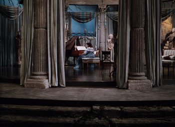 Movie still from “The Tales of Hoffmann” (1951), directed by Michael Powell – A person playing a piano in a room with columns; Extreme Wide shot, High angle