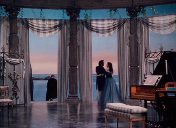 Movie still from “The Tales of Hoffmann” (1951), directed by Michael Powell – Two people standing in front of a balcony with a view of the ocean; Extreme Wide shot, High angle