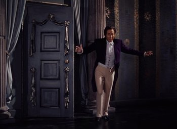 Movie still from “The Tales of Hoffmann” (1951), directed by Michael Powell – A man in a purple coat and white pants standing in front of a door; Wide shot, High angle