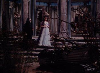 Movie still from “The Tales of Hoffmann” (1951), directed by Michael Powell – A woman in a white dress standing next to a man in a black mask; Wide shot, Low angle