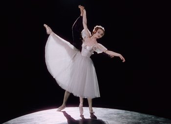 Movie still from “The Tales of Hoffmann” (1951), directed by Michael Powell – A woman in a white dress is doing a dance; Wide shot, Low angle