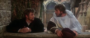 Movie still from “The Taming of The Shrew” (1967), directed by Franco Zeffirelli – Two men are sitting next to each other on a table; Medium shot, Over the shoulder angle