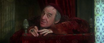 Movie still from “The Taming of The Shrew” (1967), directed by Franco Zeffirelli – An older man wearing a red hat is laying on a red couch; Close Up shot, Over the shoulder angle