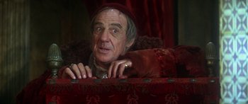 Movie still from “The Taming of The Shrew” (1967), directed by Franco Zeffirelli – An older man wearing a red hat looking at the camera; Medium shot, Over the shoulder angle