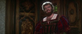 Movie still from “The Taming of The Shrew” (1967), directed by Franco Zeffirelli – A man with a beard in a red and black outfit; Medium shot, Over the shoulder angle