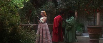 Movie still from “The Taming of The Shrew” (1967), directed by Franco Zeffirelli – Three people dressed in medieval costumes stand in a garden; Wide shot, Over the shoulder angle