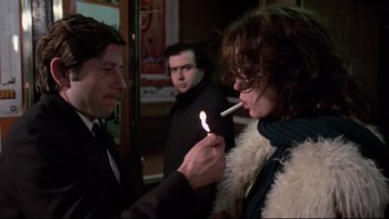 Movie still from “The Tenant” (1976), directed by Roman Polanski – A woman lighting a cigarette in front of two men; Medium shot, Over the shoulder angle