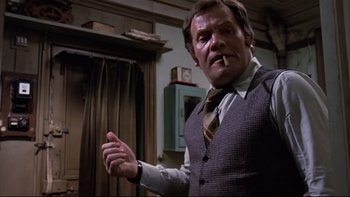 Movie still from “The Tenant” (1976), directed by Roman Polanski – A man wearing a suit and tie smoking a cigarette; Medium shot, Low angle