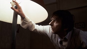 Movie still from “The Tenant” (1976), directed by Roman Polanski – A man holding onto a light in the dark; Medium shot, Low angle