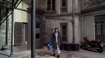Movie still from “The Tenant” (1976), directed by Roman Polanski – A man walking down the street holding a bucket of water; Wide shot, High angle