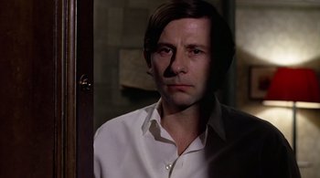 Movie still from “The Tenant” (1976), directed by Roman Polanski – A man in a white dress shirt is standing in a doorway; Close Up shot, Low angle
