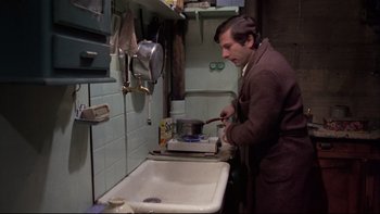 Movie still from “The Tenant” (1976), directed by Roman Polanski – A man in a brown jacket is cooking in a kitchen; Medium shot, High angle