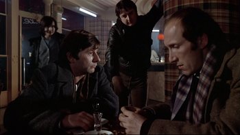 Movie still from “The Tenant” (1976), directed by Roman Polanski – A group of men sitting at a table with a glass of wine; Medium shot, Over the shoulder angle