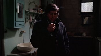 Movie still from “The Tenant” (1976), directed by Roman Polanski – A man smoking a cigarette while standing in a room; Medium shot, Over the shoulder angle