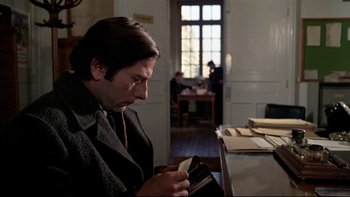 Movie still from “The Tenant” (1976), directed by Roman Polanski – A man sitting at a table looking at a wallet; Medium shot, Low angle